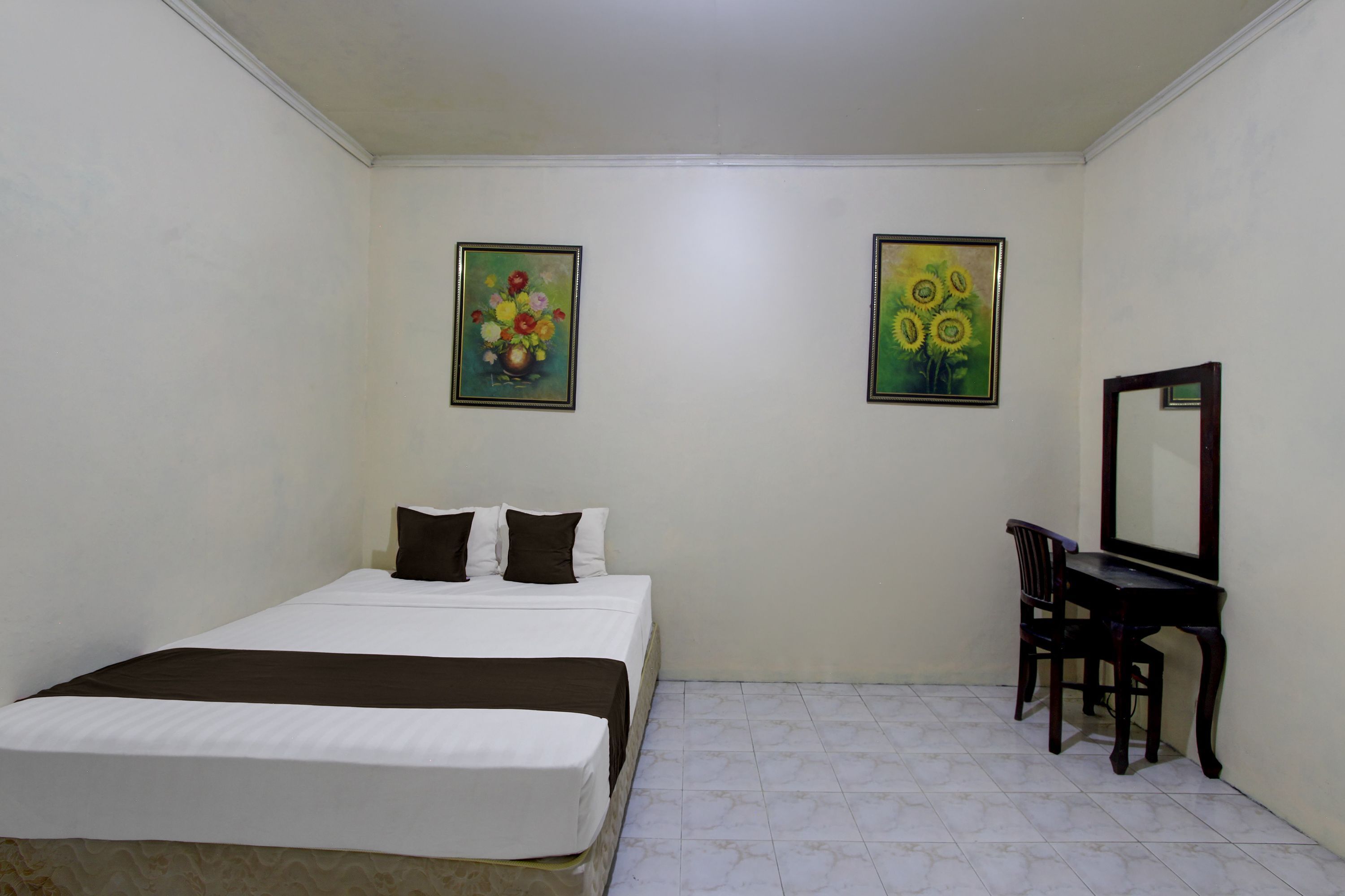 A bedroom with a bed, a desk, and two paintings on the wall.