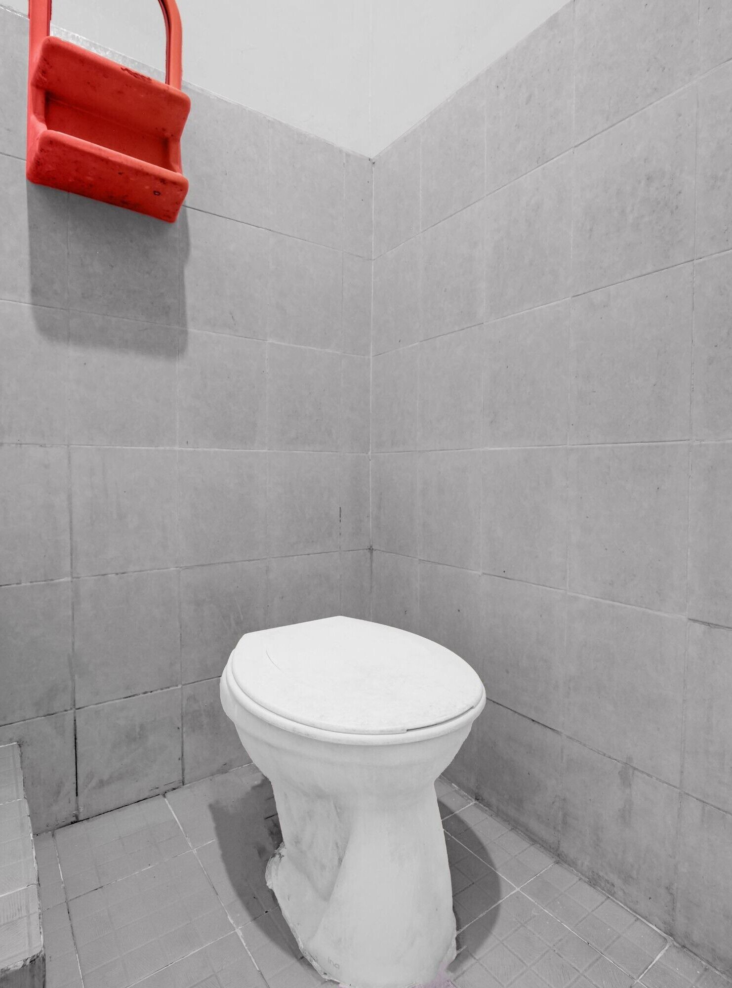 A bathroom with a toilet, grey tiles, and a red object on the wall.