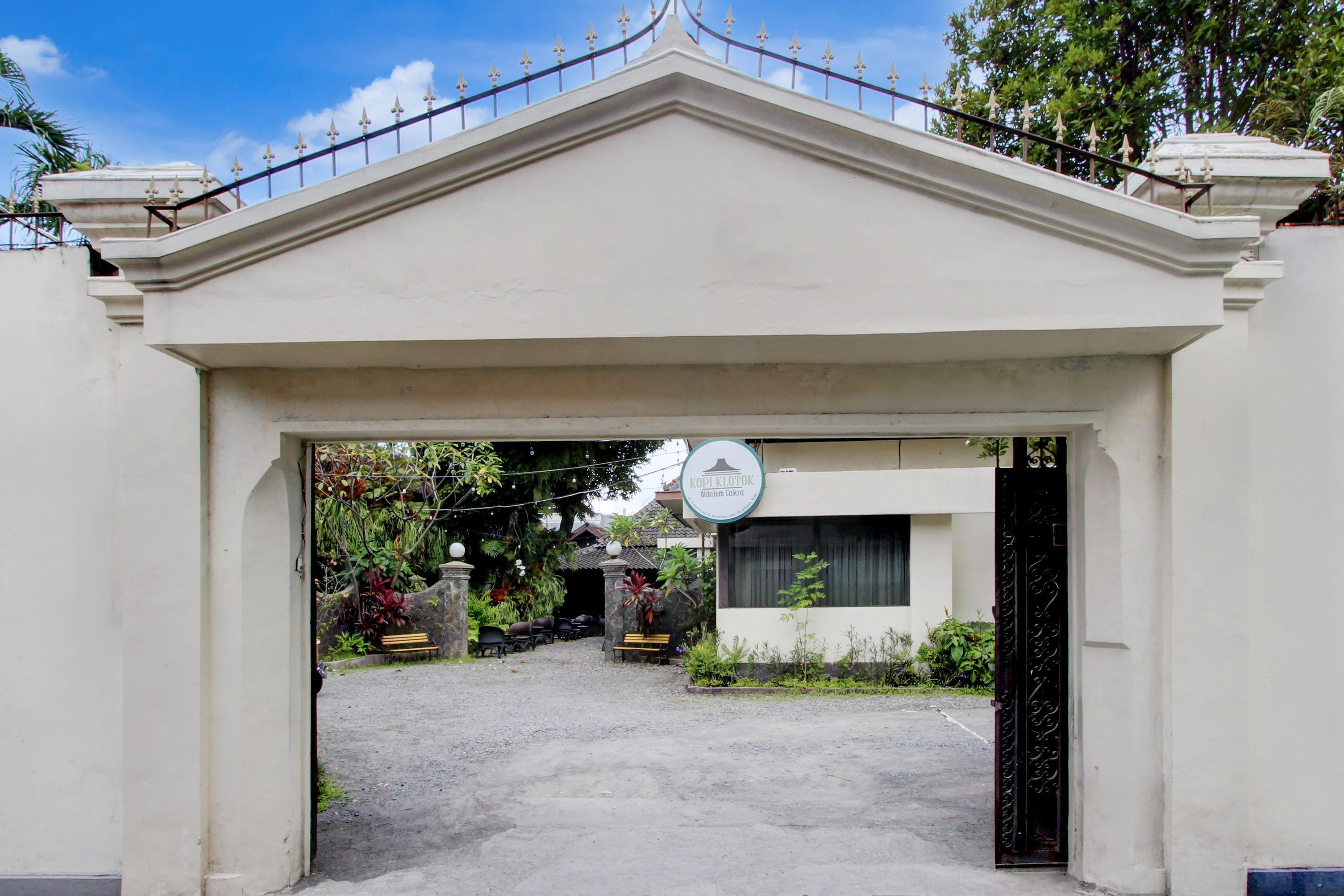 A gated entrance with a sign, a paved driveway, and a building with a white facade.