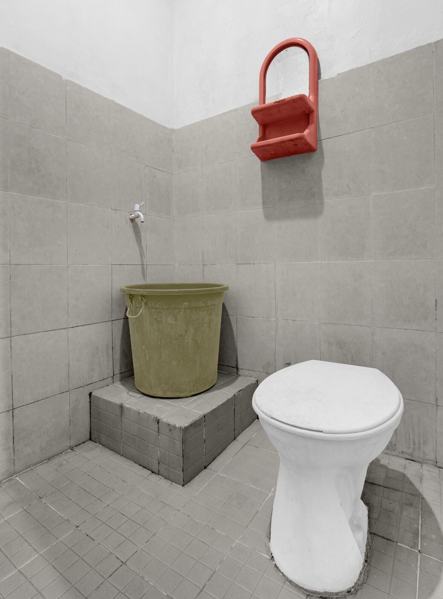 A bathroom with a white toilet, a green bucket, and a red faucet.