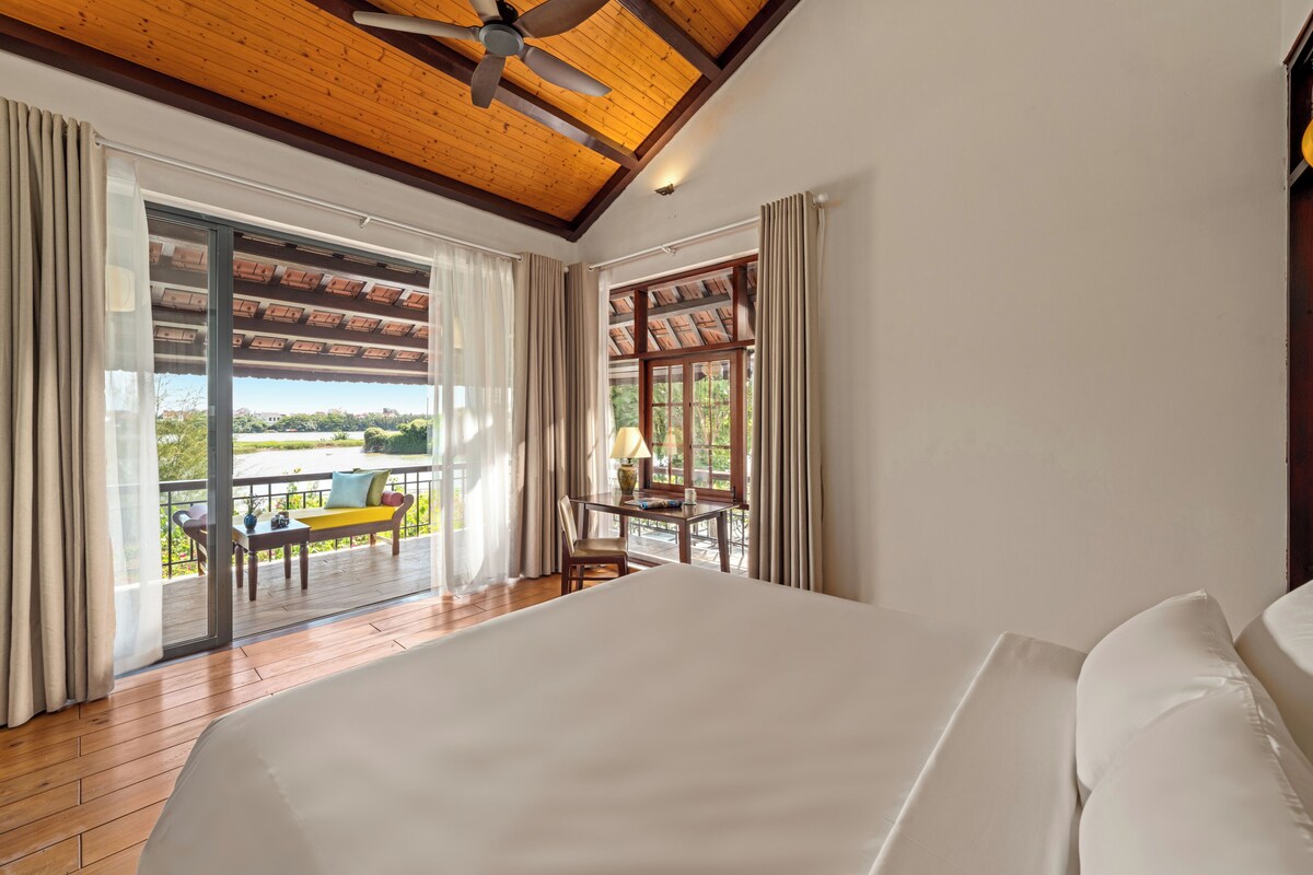 A bedroom with a large bed, a ceiling fan, and a view of a balcony with outdoor furniture.