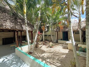 Un patio con construcciones de techo de paja, palmeras y suelo arenoso.