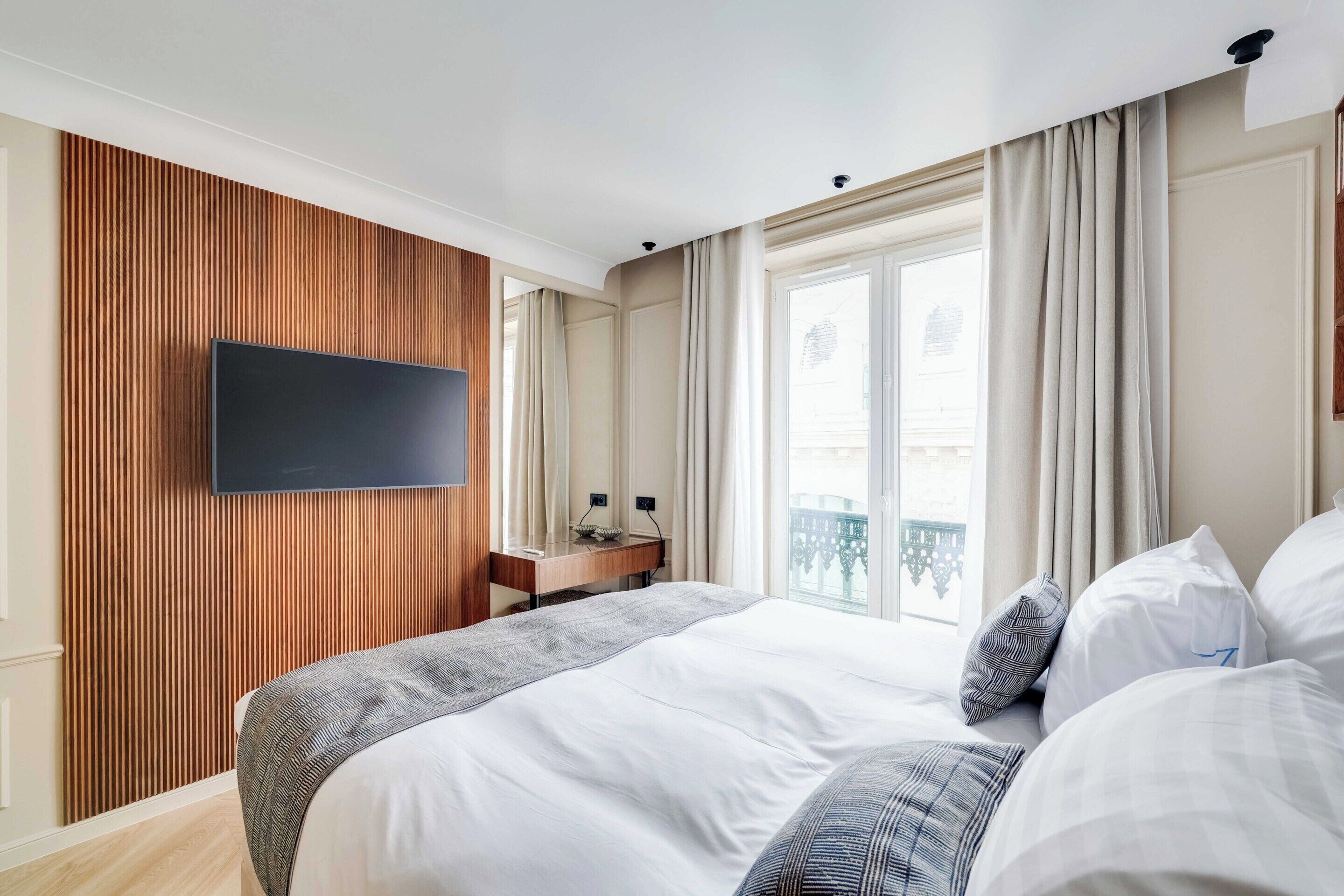 Ein Hotelzimmer mit einem großen Bett, einem flachbildfernseher an der Wand, einem Schreibtisch mit Stuhl und einem Fenster mit Vorhängen.