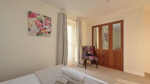 Une chambre à coucher avec un lit, une chaise, une armoire en bois, un tableau et une fenêtre avec des rideaux.