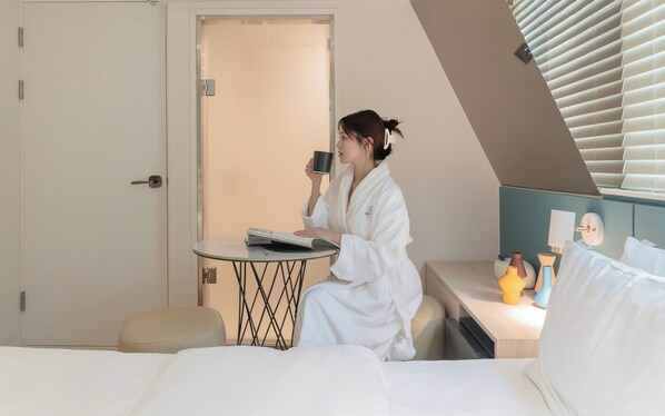 A hotel room with a bed, a small round table with a book and a cup, a bedside table with decorative items, and a door leading to another room. - Sinchon APL Hotel (Seoul)