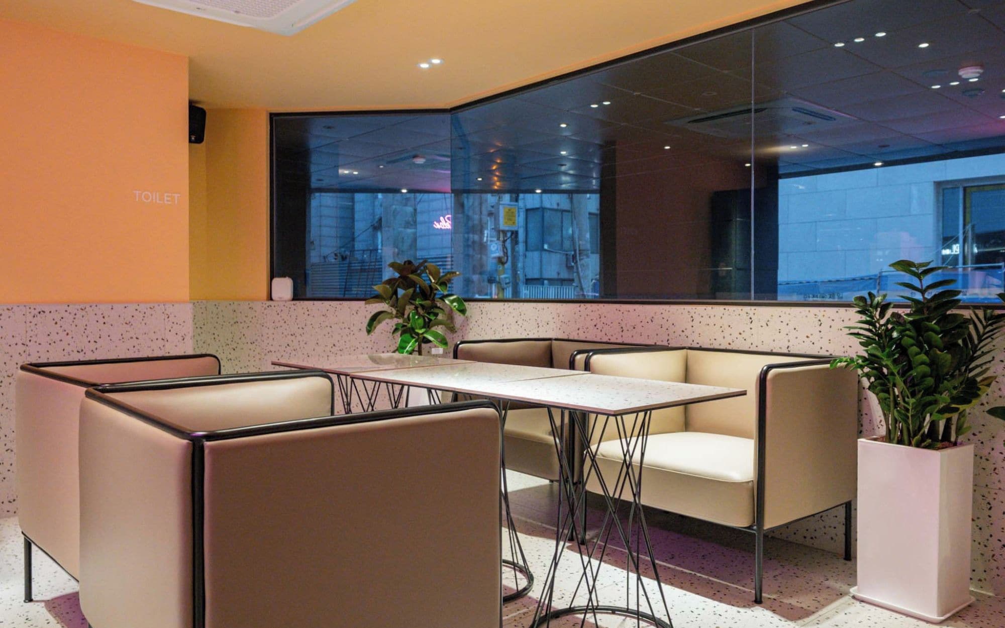 A modern meeting room with a glass wall, a table, chairs, and potted plants.