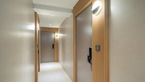 Un corridoio con una porta in legno, un interruttore della luce e un lampadario.