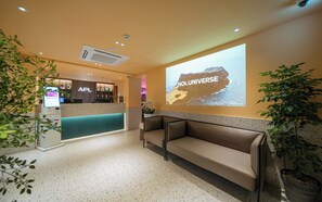 Zona de recepción de un hotel con un quiosco digital, un mostrador de recepción, un área de descanso y una pantalla de proyección que muestra 'NOL UNIVERSE'.