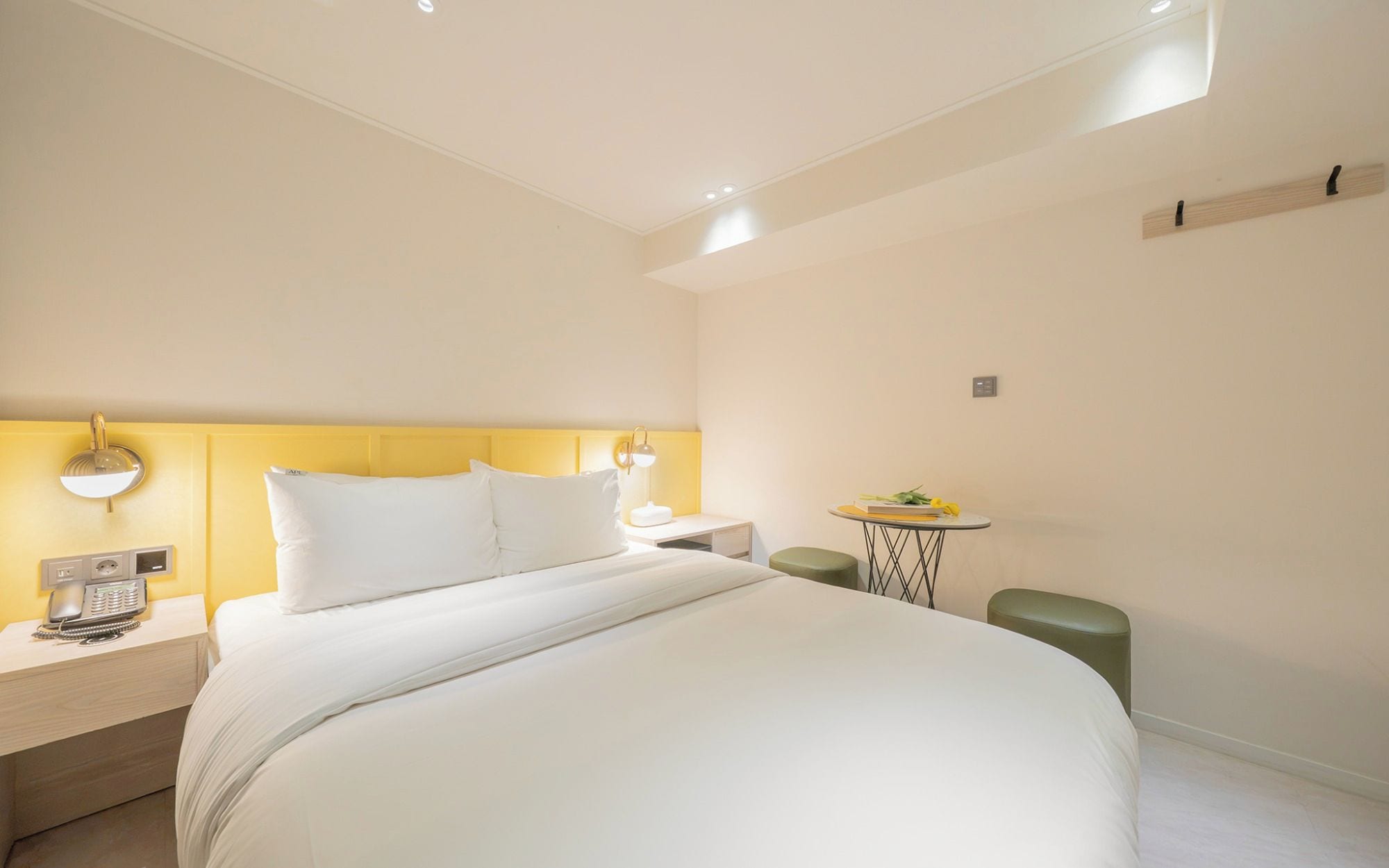 A hotel room with a large bed, bedside tables, a small table with a lamp, and a green ottoman.