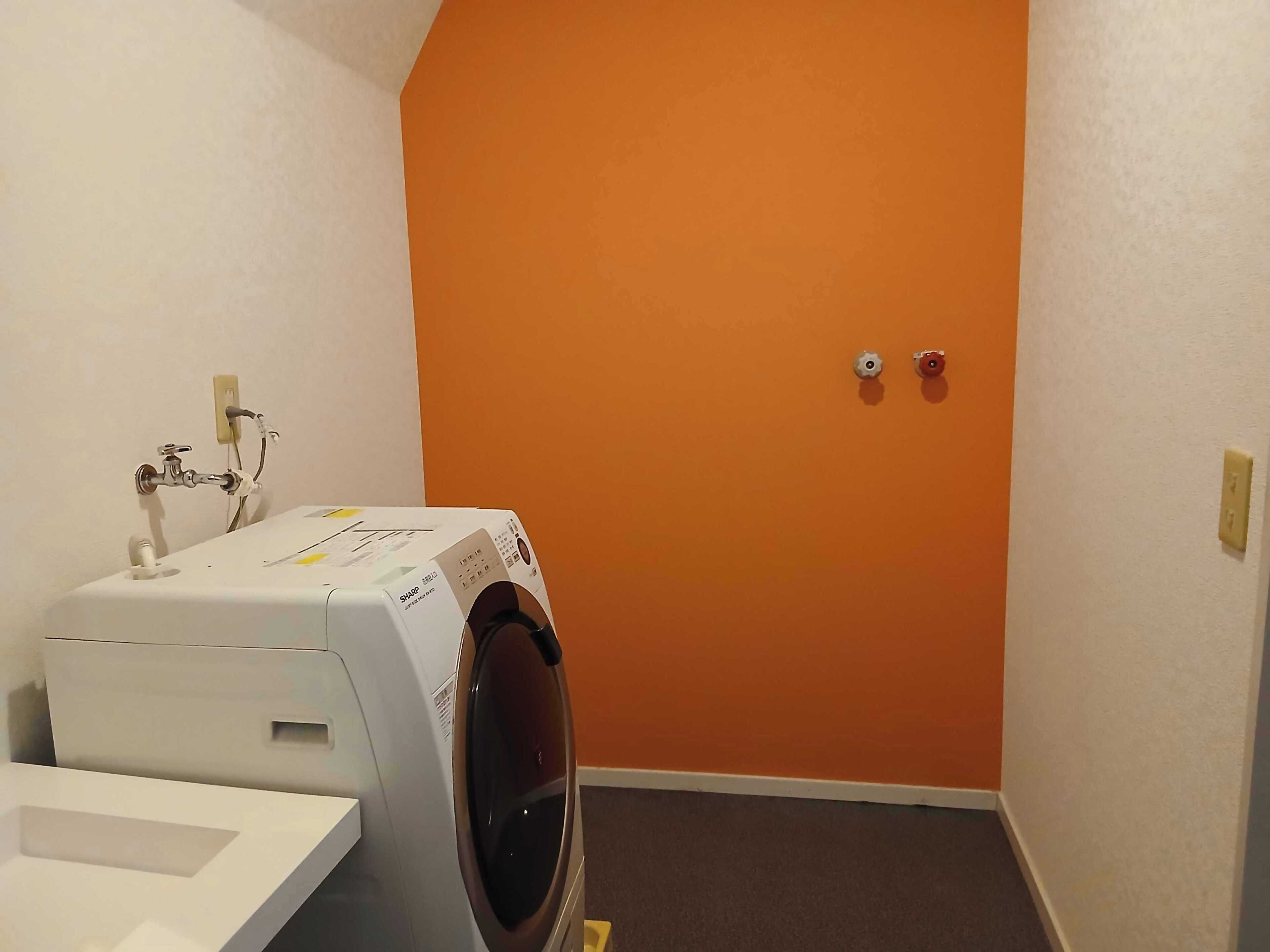 Een wasserette met een wasmachine, een wit wastafel en een oranje muur.