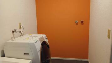 Een wasserette met een wasmachine, een wit wastafel en een oranje muur.