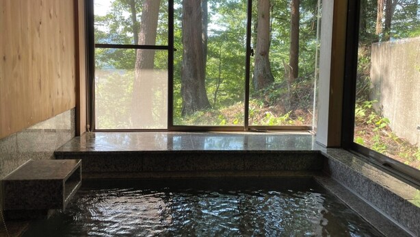 Un espace de détente avec un banc en pierre et un jacuzzi, le tout entouré de grandes fenêtres offrant une vue sur la forêt.