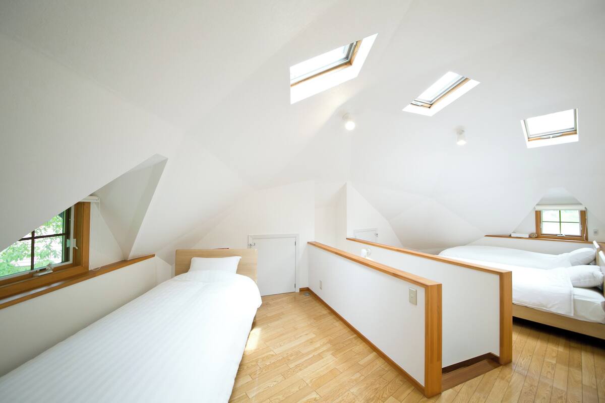 A modern, well-lit bedroom with skylights, a wooden floor, and a simple, clean design.