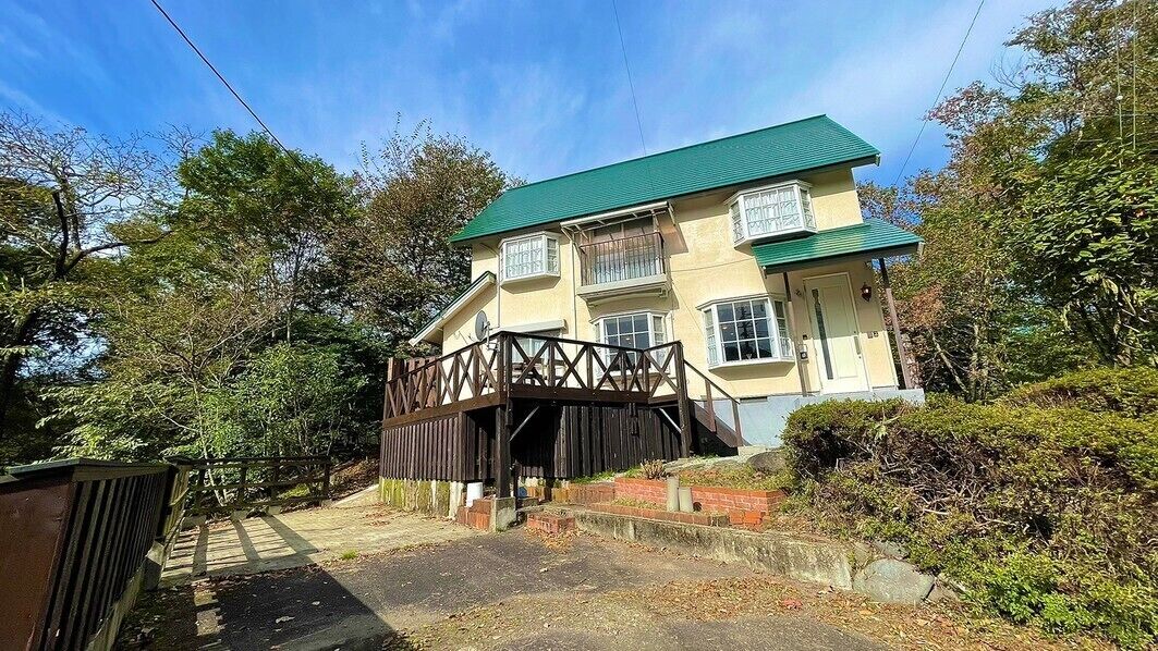A two-story building with a green roof, a wooden bridge, and a paved driveway.