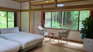 Une chambre avec deux lits, une petite table, deux chaises et une grande fenêtre donnant sur la forêt.