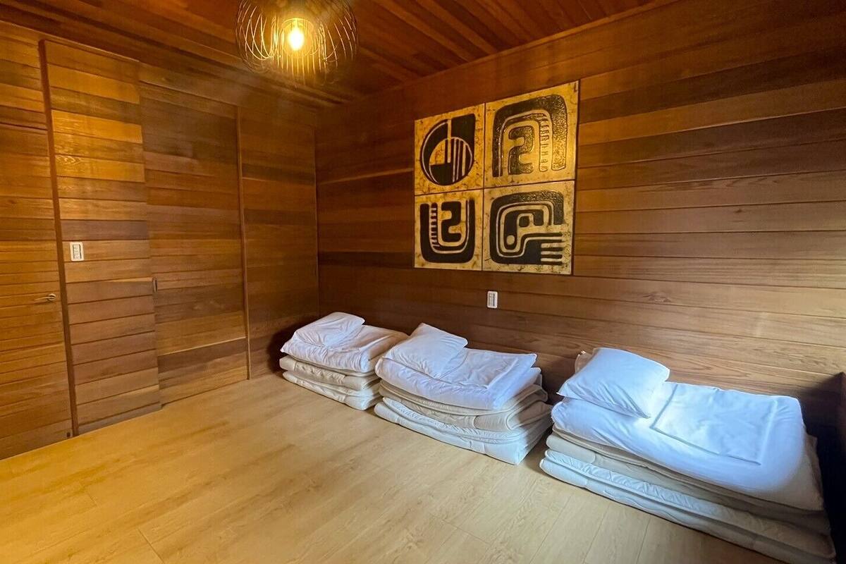 A sauna room with wooden walls, a wooden floor, and a wall-mounted heater. There are four benches with folded towels.