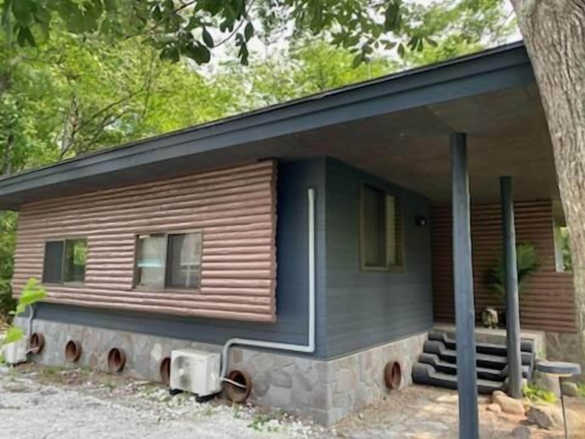 A cabin with a log exterior, a porch, and a stone foundation.