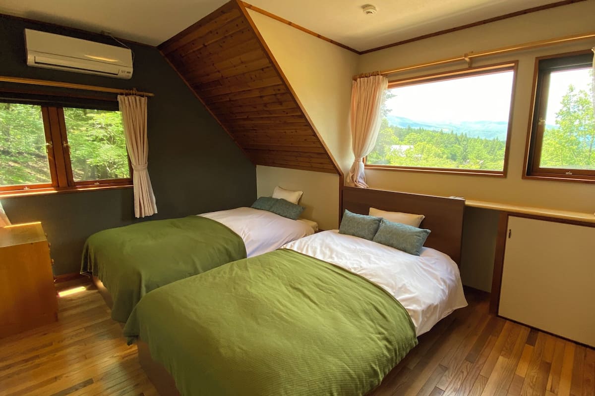 A room with two beds, a small cabinet, and a window with curtains.