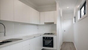 A compact kitchen with white cabinets, a gas stove, a built-in oven, and a stainless steel sink. - Luxury Granny Cottage Retreat in arms reach of Golf Course (Wilton)