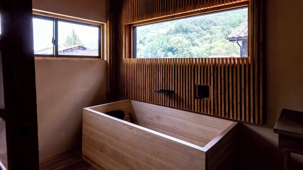 Una bañera de madera con una ventana encima, un banco de madera y paneles de madera en la pared.
