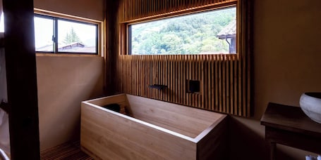 A wooden bathtub with a window above it, a wooden bench, and a wooden wall paneling.