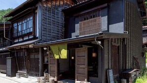 Un edificio japonés tradicional con varios pisos de madera, puertas correderas y una zona de entrada cubierta.