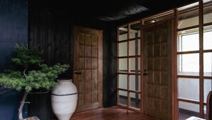 Una habitación japonesa tradicional con puerta de madera, puertas correderas de vidrio, un árbol en maceta y un jarrón grande.