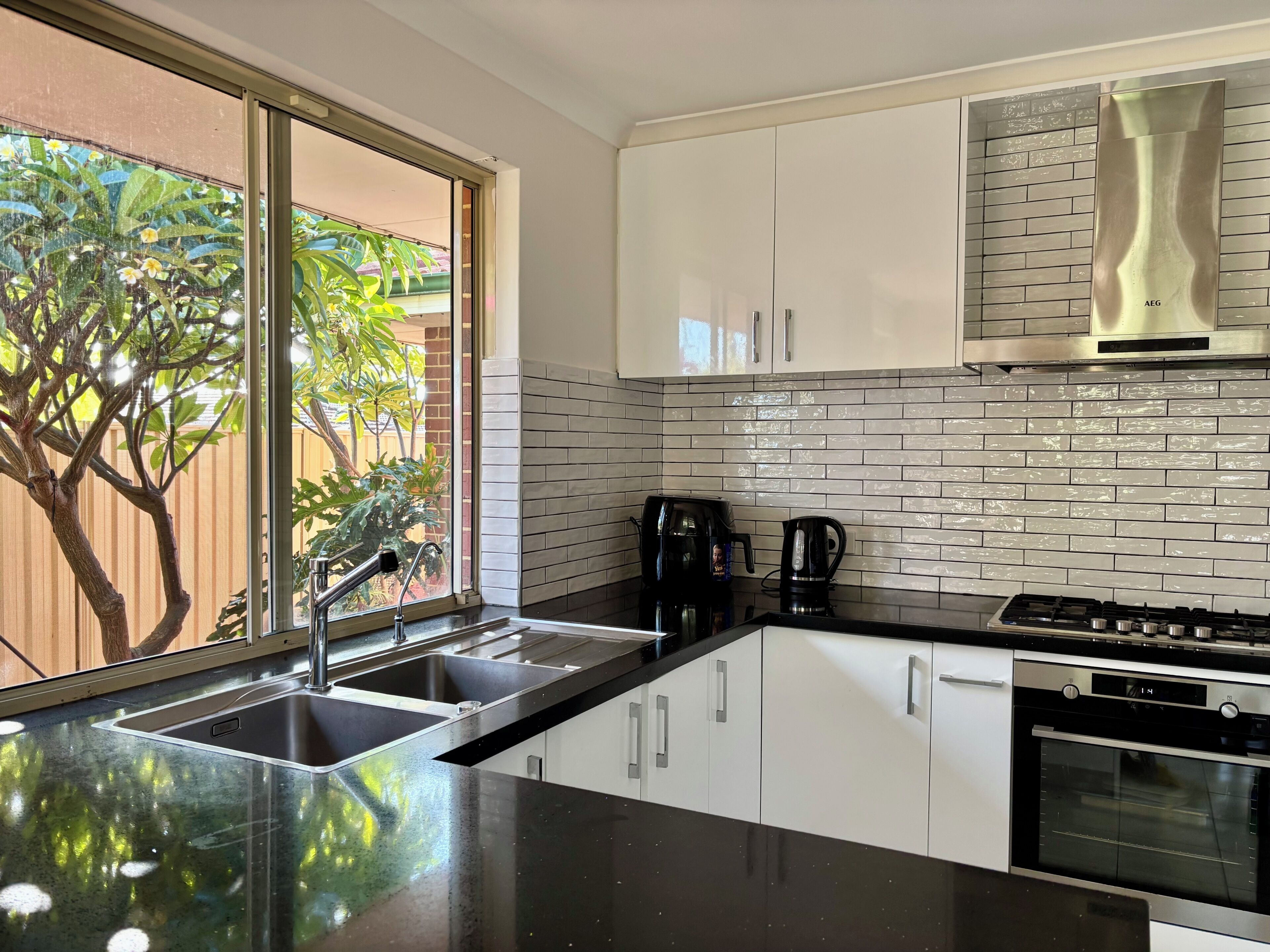 A modern kitchen with a large window, stainless steel appliances, and white cabinetry.