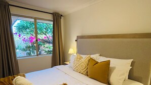 Une chambre d’hôtel avec un lit, une fenêtre, une table de chevet et une vue sur la verdure environnante.