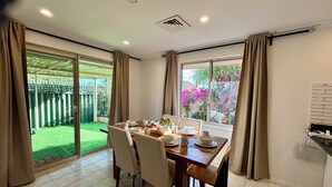 Un coin repas avec une table dressée pour quatre personnes, de grandes fenêtres et une vue sur un jardin.