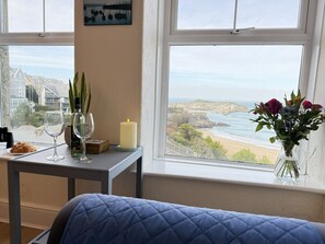 A room with a bed, a table with a candle, a vase of flowers, and a view of the sea and buildings. - Draycott Dreams has stunning sea views across St Ives Bay & Harbour (St Ives)