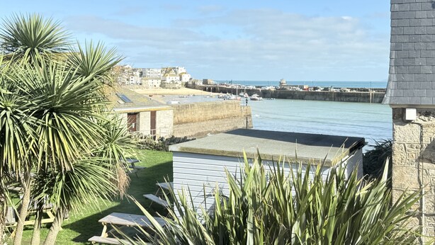 A coastal view with a stone wall, a grassy area with picnic tables, and a distant town. - Coasters House a spacious St Ives townhouse in the hidden quarter (St Ives)