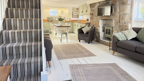 A staircase with striped carpet, a living room with a sofa and a fireplace, and a kitchen with a stone wall and a TV. - Coasters House a spacious St Ives townhouse in the hidden quarter (St Ives)
