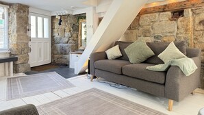 A cozy living area with a stone wall, a sofa with cushions, and a staircase. - Coasters House a spacious St Ives townhouse in the hidden quarter (St Ives)