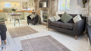 A modern living room with a stone fireplace, a grey sofa, and a dining area with a white table and chairs. - Coasters House a spacious St Ives townhouse in the hidden quarter (St Ives)
