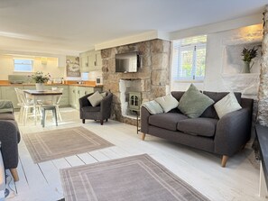 A modern living room with a stone fireplace, a grey sofa, and a dining area with a white table and chairs. - Coasters House a spacious St Ives townhouse in the hidden quarter (St Ives)