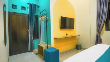 Una habitación con cama, televisor montado en la pared, puerta, zona de ducha y un taburete pequeño.