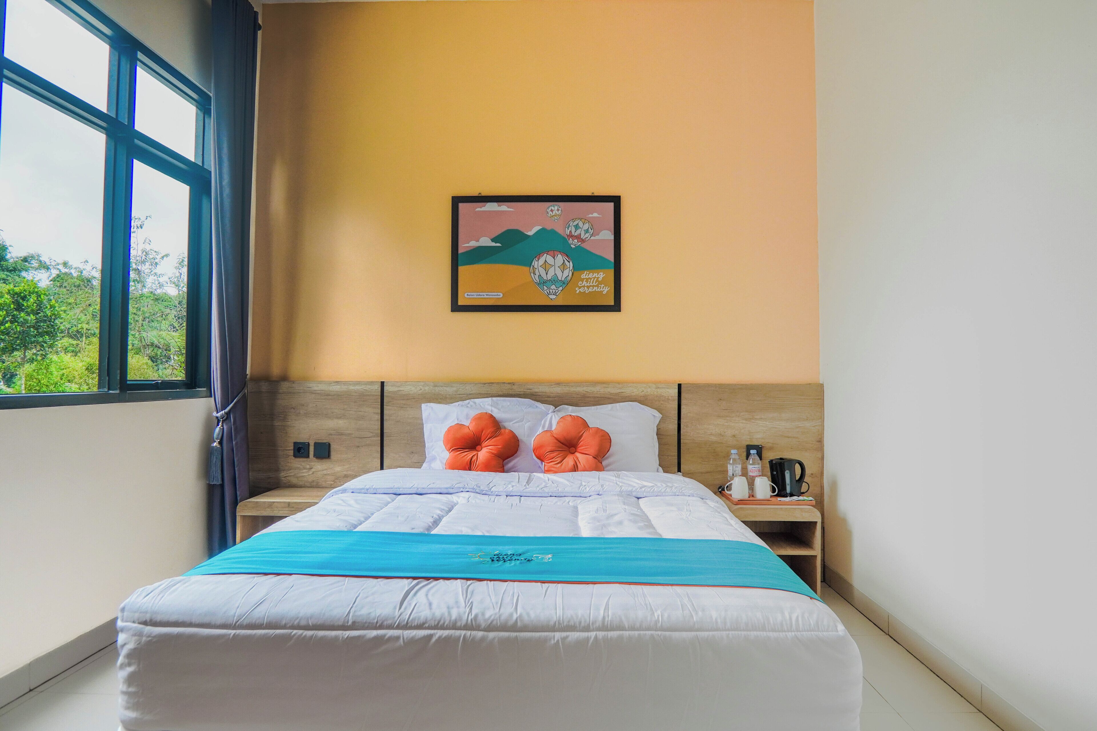 A hotel room with a bed, pillows, a nightstand, a framed picture, and a window.