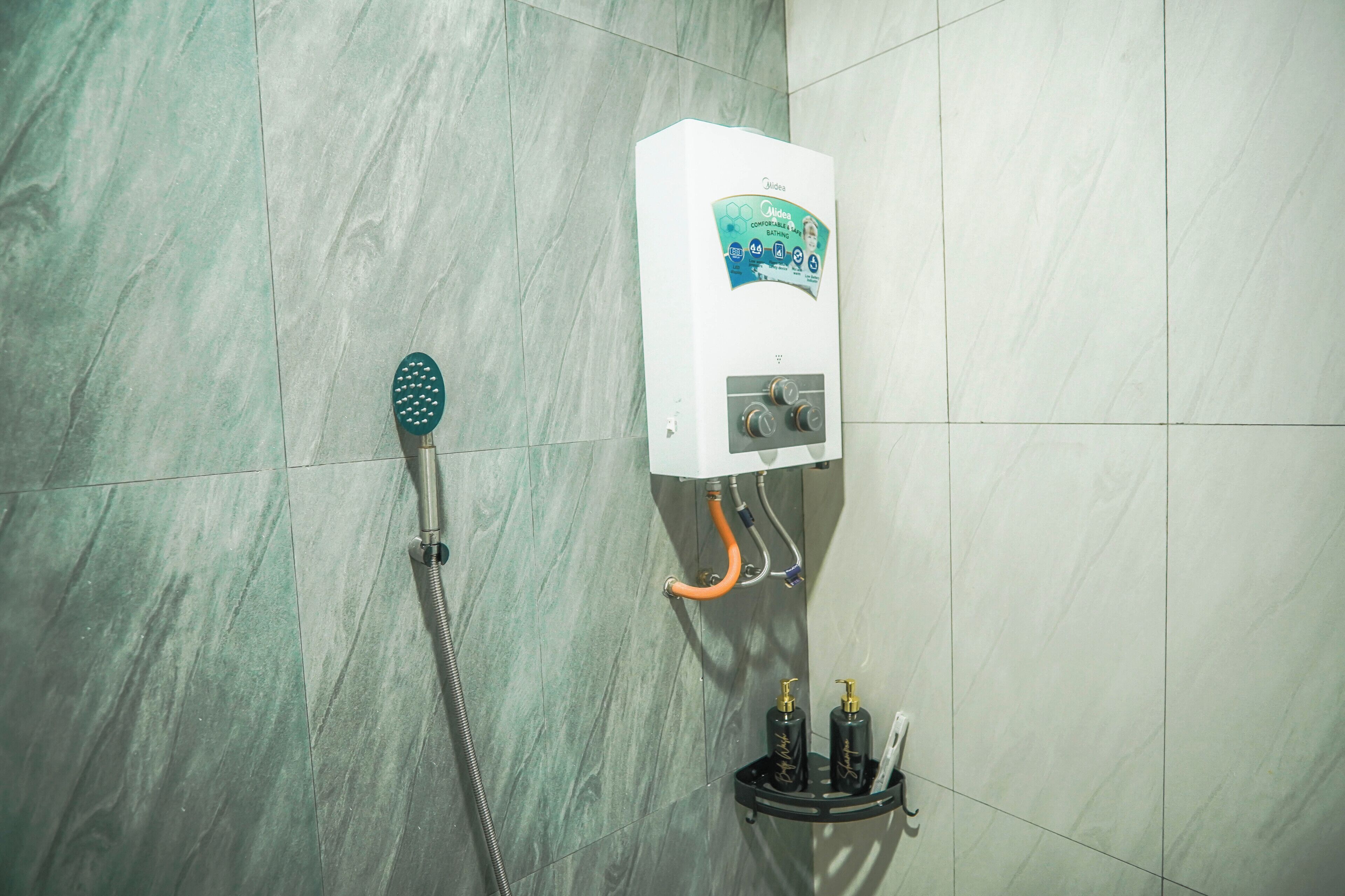 Un baño con ducha, calentador de agua y dos botellas en una estantería.