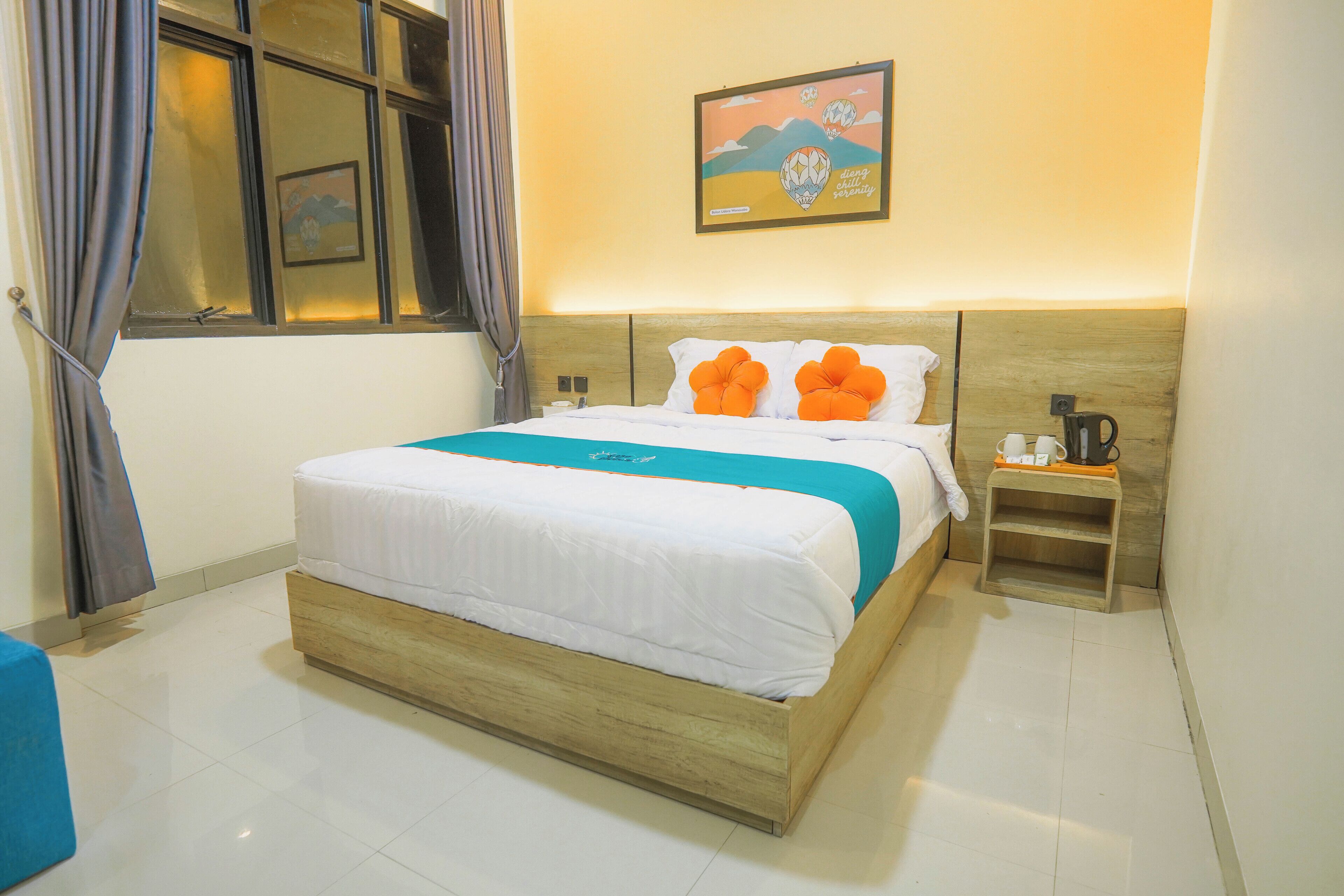 Habitación de hotel con cama de madera, ropa de cama blanca, almohadas naranjas, una mesita de noche con cafetera y un cuadro en la pared.