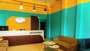 A reception area with a reception desk labeled 'RECEPTIONIS,' a brown sofa, two small tables with plants, and a wall with a decorative sign. - INSTAY Hotel Dieng Chill Serenity (Garung)