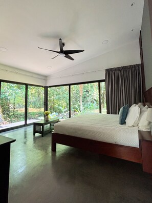 Ein Schlafzimmer mit Bett, Schreibtisch, Deckenventilator und großen Fenstern.