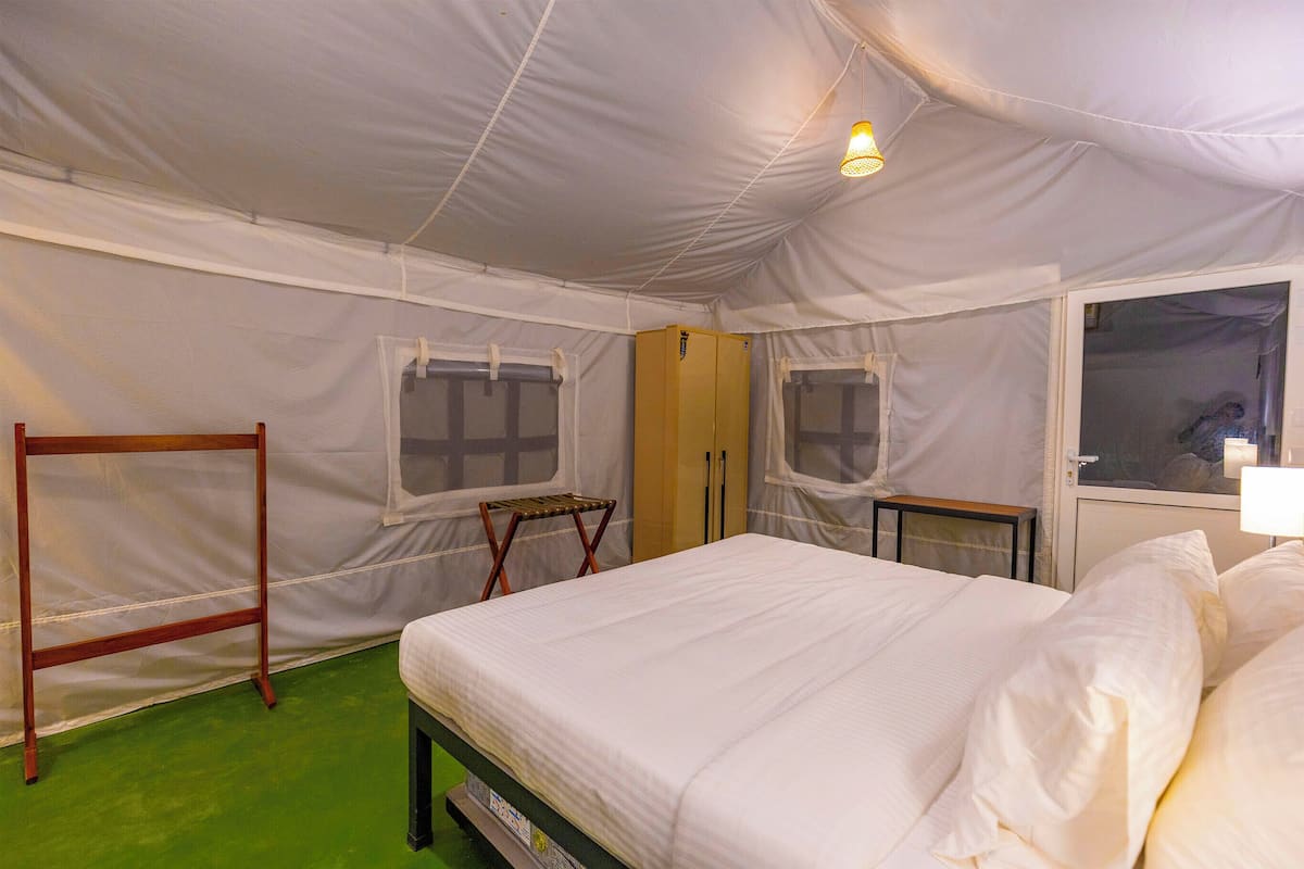 A tented room with a bed, windows, a wardrobe, and a small table.