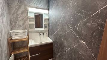 A bathroom with a marble wall, a sink, a mirror, and a wooden shelf with a basket.