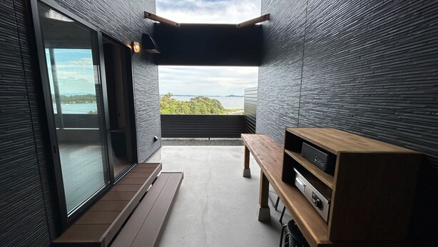 Un interior moderno con un ventanal corredera que da a un balcón, un banco de madera y un mueble empotrado para entretenimiento.