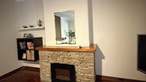 Quarto com lareira de pedra, espelho fixado na parede, estante de livros e televisão.