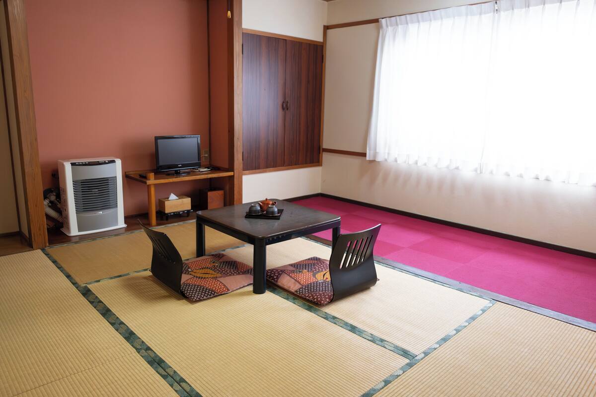 Una habitación con tatami, televisor, calentador y ventana con cortinas.