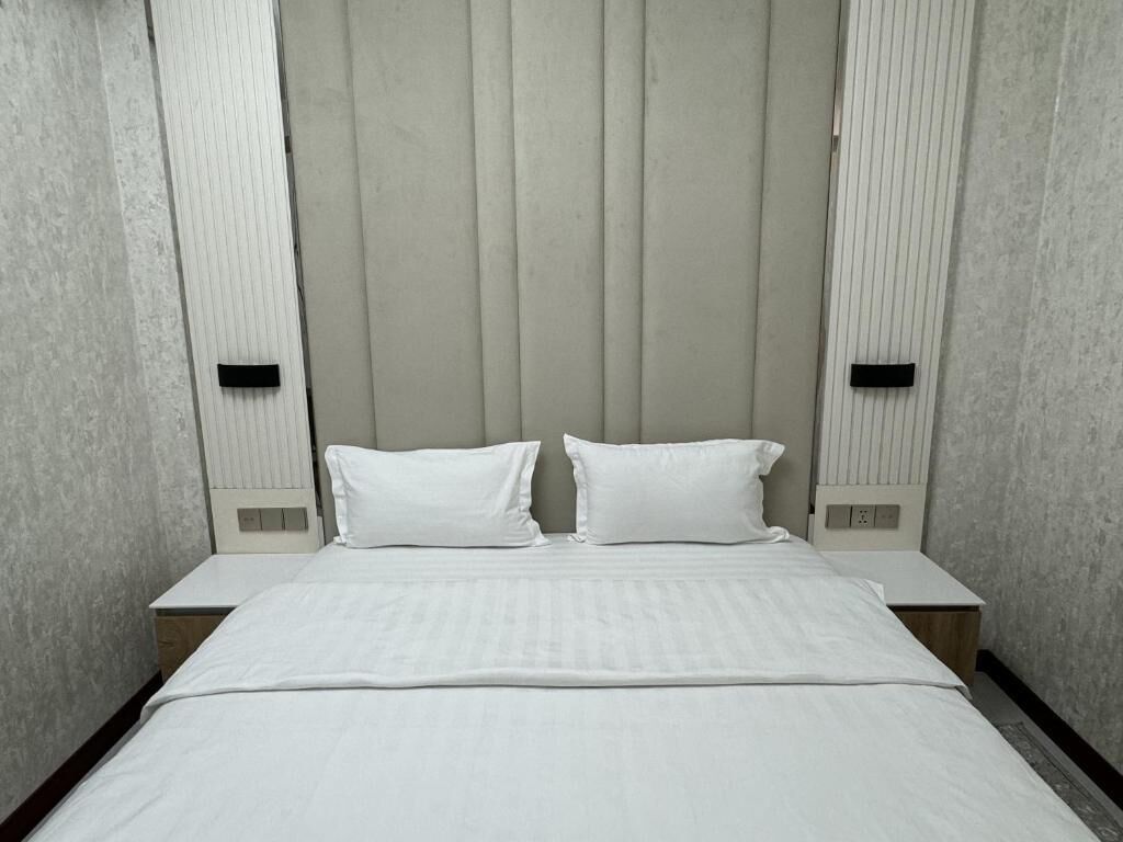 Una habitación de hotel con una cama, dos mesitas de noche y un cabecero con líneas verticales.