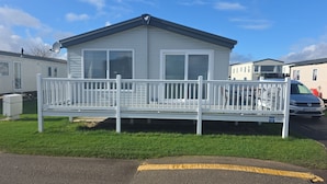Ett enplanshus på hjul med vit fasad, en veranda med ett vitt räcke och ett fordon parkerat på uppfarten.
