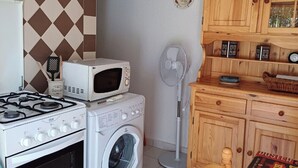 Eine kleine Küche mit Gaskochfeld, Mikrowelle, Waschmaschine und Holzausstattung.